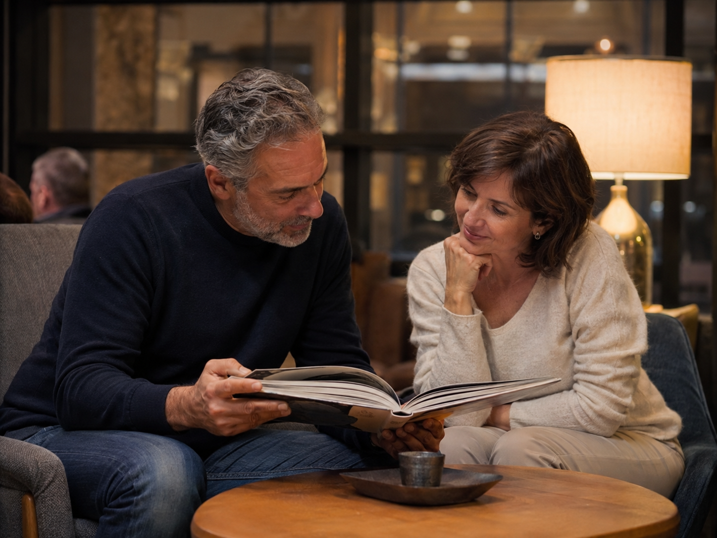 Adult showing another a travel album in a quiet public lounge.