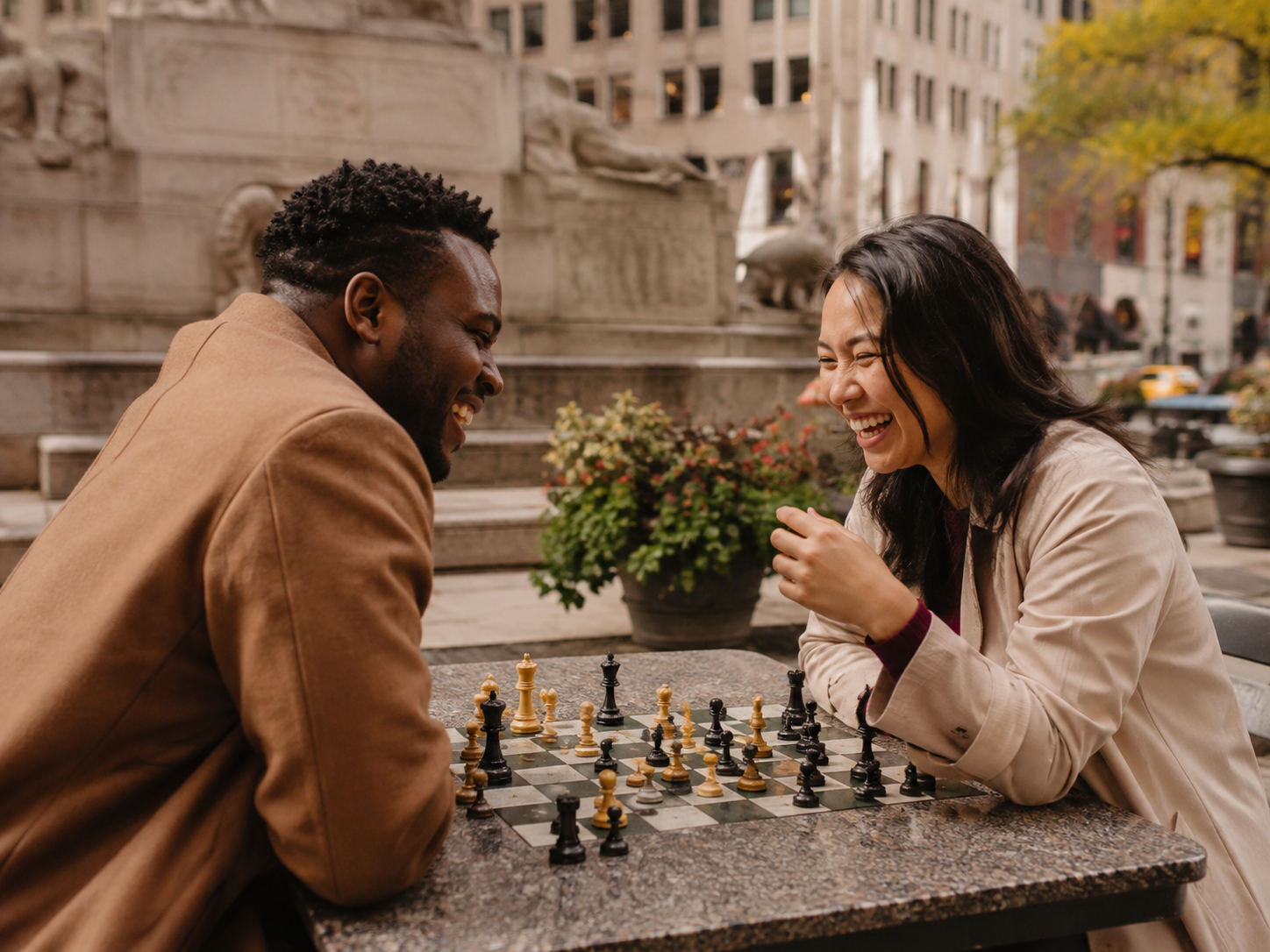 Two adults laughing at a chess table in a public plaza.